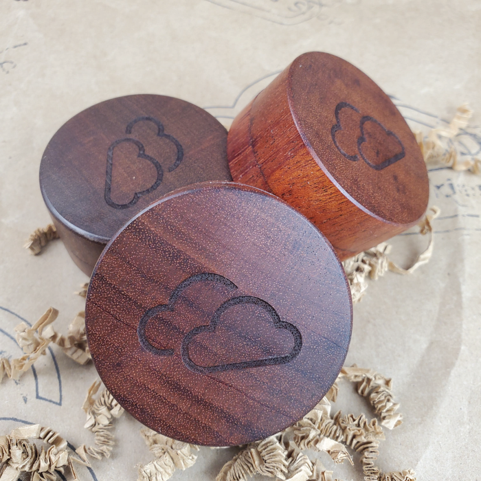 SAPELE WOOD HERB GRINDER WITH CLOUD LOGO ON CRINKLE PAPER AND THE 9TH CLOUD CANNABIS ACCESSORIES SHIP LOGO BACKGROUND